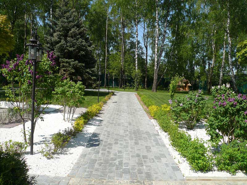 Однотипные партерные клумбы обрамляют дом со всех сторон. За счет подбора декоративных кустарников они выглядят торжественно и гармонично с ранней весны до поздней осени.