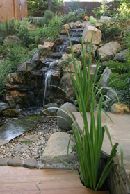 Высота водопада 3,5м. Глыбы камня уложены каскадом. Для предотвращения оползания склон фиксирован подпорными стенками и крупными камнями. 